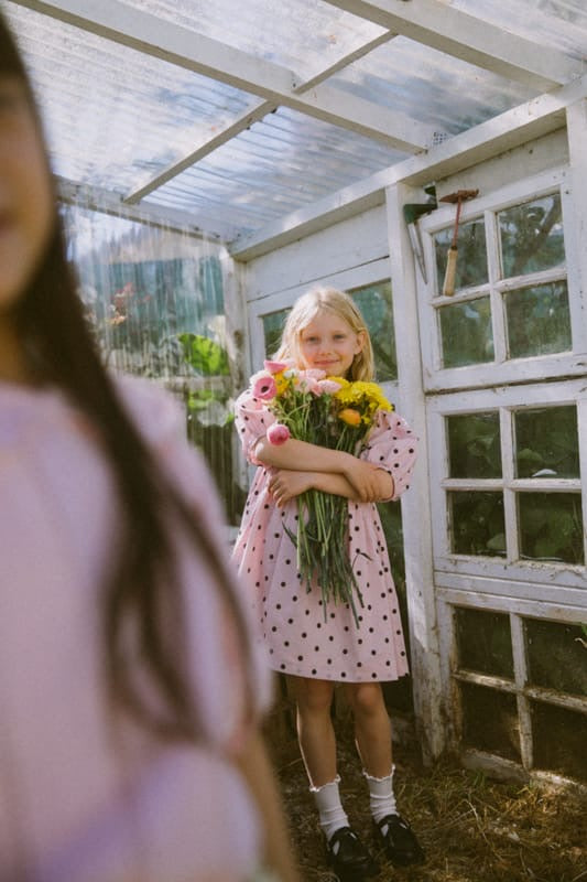 Young girl holding flowers in a greenhouse. wearing pink dress with black spots sun is shining 