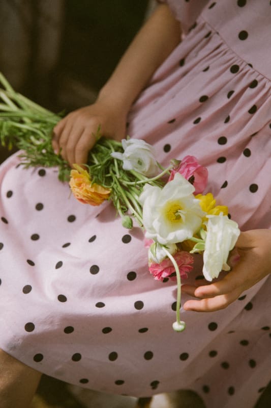 child wearing a pink polka dot dress holding a bouquet of flowers.